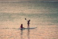 Sunset scene on background. Two little girls silhouettes are padddling