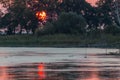 Sunset scene over lake, with sun coming down behind some trees and reflecting on water Royalty Free Stock Photo