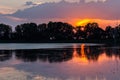 Sunset scene over lake, with sun coming down behind some trees and reflecting on water Royalty Free Stock Photo