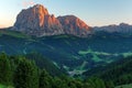 Sunset scenery of rugged Sassolungo-Sassopiatto mountains with alpenglow & a village in green grassy valley