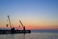Sunset at sea, evening at sea. against the background of a beautiful sky, a silhouette of a pier with lifting mechanisms