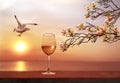Sunset at sea glass of white wine and seagull fly ,  spring flowers branch seascape horizon ,sun down ,summer leisure vacation  na Royalty Free Stock Photo