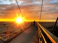 Sunset at sea maritime bridge gate in the sun light beach people walking romantic couple stay on sand reflection on sea water wa