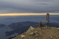 Sunset on the sea with pouring bright sun rays through the clouds. A chair on top of a mountain