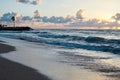 Sunset at the sea. Turquoise water in the ocean in the evening. Yellow sky with small clouds and blue waves at sandy beach at the