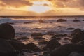 Sunset seen from the shore with black and round rocks in the foreground