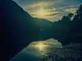 Cross shaped sunset over the mountains and reflection on water below.