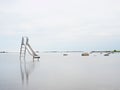 Sunset shore and old steel slide in lake. Chrome ladder tower with sliding track, big granite stone Royalty Free Stock Photo