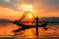 Sunset silhouette Asian fisherman on a wooden boat casts nets