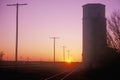 Sunset silhouette of grain silo beside train tracks, KS