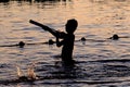 Sunset silhouette of happy child enjoys water games in the pool