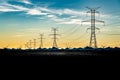 Sunset silhouette of steel lattice transmission towers and power lines overlooking distant mountains and windmills Royalty Free Stock Photo