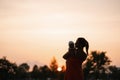 Sunset Silhouette: Young mother holding her baby boy child in city park standing in front of setting sun and vivid