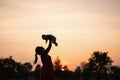 Sunset Silhouette: Young mother holding her baby boy child in city park standing in front of setting sun and vivid