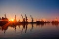 Sunset silhouettes shipping cranes at busy port. Commercial cargo docks during golden hour, sun reflections on water Royalty Free Stock Photo