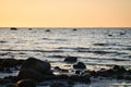 Sunset, stone beach with small and large rocks in front of the illuminated sea Royalty Free Stock Photo