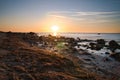 Sunset, stone beach with small and large rocks in front of the illuminated sea Royalty Free Stock Photo