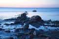 Sunset, stone beach with small and large rocks in front of the illuminated sea Royalty Free Stock Photo