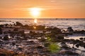 Sunset, stone beach with small and large rocks in front of the illuminated sea Royalty Free Stock Photo