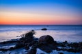 Sunset, stone beach with small and large rocks in front of the illuminated sea Royalty Free Stock Photo