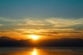 Sunset-Sun sets behind the mountains and over water with reflection Royalty Free Stock Photo