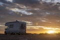 Sunset / sunrise at rocky seaside with travel trailer with bike. Dramatic and calm cloudy sky with sun beams Royalty Free Stock Photo