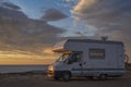 Sunset / sunrise at rocky seaside with travel trailer with bike. Dramatic and calm cloudy sky with sun beams Royalty Free Stock Photo