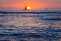 Sunset surfers and sailboats