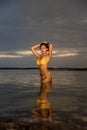Sunset time on the beach. Attactive Asian woman posing in yellow bikini. Tanned skin. Slim fit body. Water reflaction. Tropical