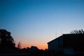 Sunset in the tropics - a dark blue sky with a strip of red setting sun against the background of houses, plants and palm trees Royalty Free Stock Photo