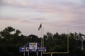 Sunset view of football end zone with goal posts, American flag flying and score board during evening Royalty Free Stock Photo