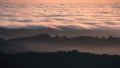 Sunset view of layered hills and valleys covered by a sea of clouds in Santa Cruz mountains; paraglider visible above the clouds; Royalty Free Stock Photo