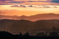 Sunset view of layered hills and valleys in Santa Cruz mountains; clouds covering the sky and the Pacific Ocean visible in the