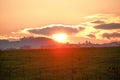 Sunset view over the field red sun setting behind clouds making sky golden