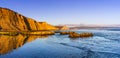 Sunset view of the Pacific Ocean shoreline, with golden colored cliffs reflected on the wet sand, Drakes Beach, Point Reyes