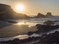 Sunset view of sand beach Praia da Zambujeira do Mar with rock and cliff, small stream and the setting sun to the ocean