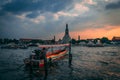 Sunset at Wat Arun. Chao Phraya with Longboat at Sunset. View from a Restaurant with some tourists inside.