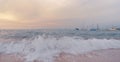 At sunset the waves break on the beach in front of boats Royalty Free Stock Photo