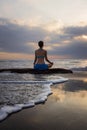 Sunset yoga. Caucasian woman sitting on the stone in Lotus pose. Padmasana. Hands in gyan mudra. Beach in Bali. View from back.