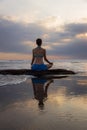 Sunset yoga. Caucasian woman sitting on the stone in Lotus pose. Padmasana. Hands in gyan mudra. Beach in Bali. View from back. Royalty Free Stock Photo