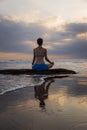 Sunset yoga. Caucasian woman sitting on the stone in Lotus pose. Padmasana. Hands in gyan mudra. Beach in Bali. View from back. Royalty Free Stock Photo