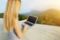 Sunshine photo of young girl using laptop, mountains in background, Thailand.