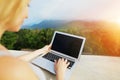 Sunshine photo of young woman using laptop, mountains in background, Bali.