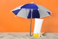 Suntan product and starfish under beach umbrella on sand against orange background Royalty Free Stock Photo