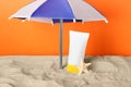 Suntan product and starfish under beach umbrella on sand against orange background Royalty Free Stock Photo