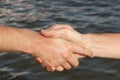 Suntanned male hands make handshake against a water surface Royalty Free Stock Photo