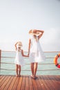 Suntanned woman and girl in white dresses enjoy sea view at the wooden pier