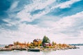 Suomi Or Finland. Beautiful Red Finnish Wooden Log Cabin House On Rocky Island Coast In Summer Sunny Evening. Lake Or