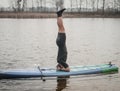 SUP YOGA, a man in a wetsuit doing yoga on a cloudy day, headstand on a paddle Board Royalty Free Stock Photo