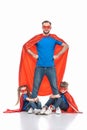 super dad standing with hands on waist and looking at camera while kids hugging his legs Royalty Free Stock Photo